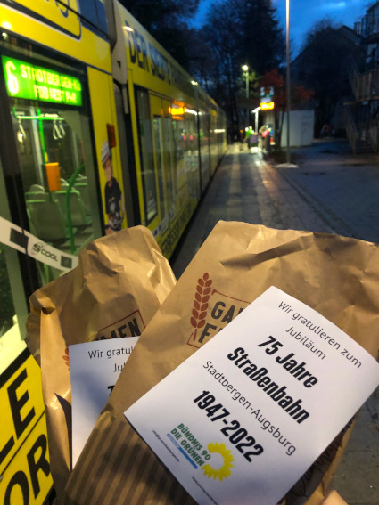 Bild einer Brezentüte mit Glückwunsch zum Jubiläum, im Hintergrund eine Straßenbahn
