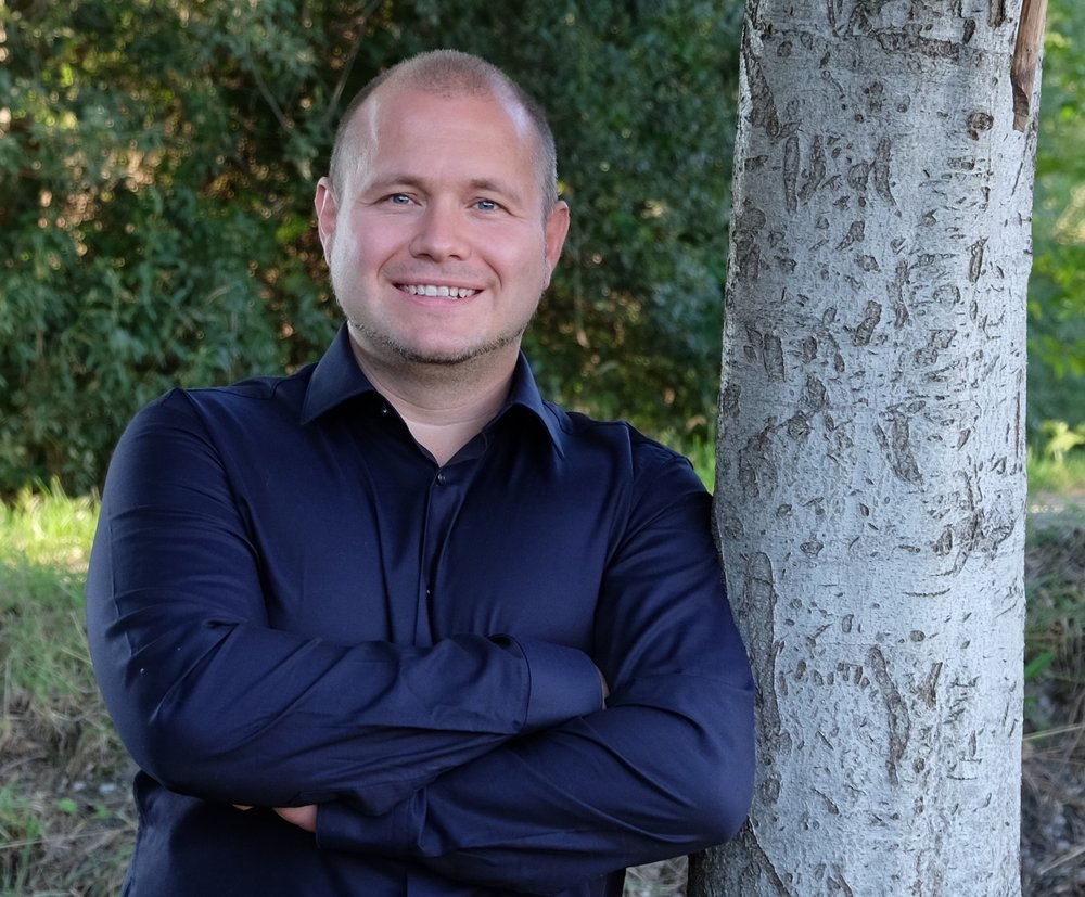 GRÜNER Landratskandidat Felix Senner lehnt im blauen Hemd an einem Baum