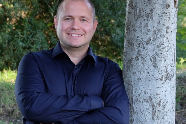 GRÜNER Landratskandidat Felix Senner lehnt im blauen Hemd an einem Baum